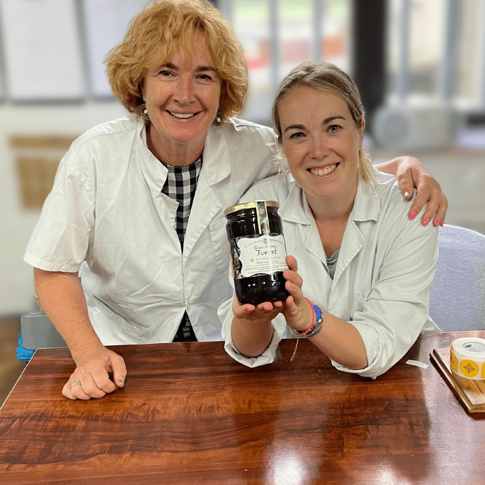 Beekeepers Luisa and her daughter Olaya in white coats. Olaya holds large glass jar of dark honey