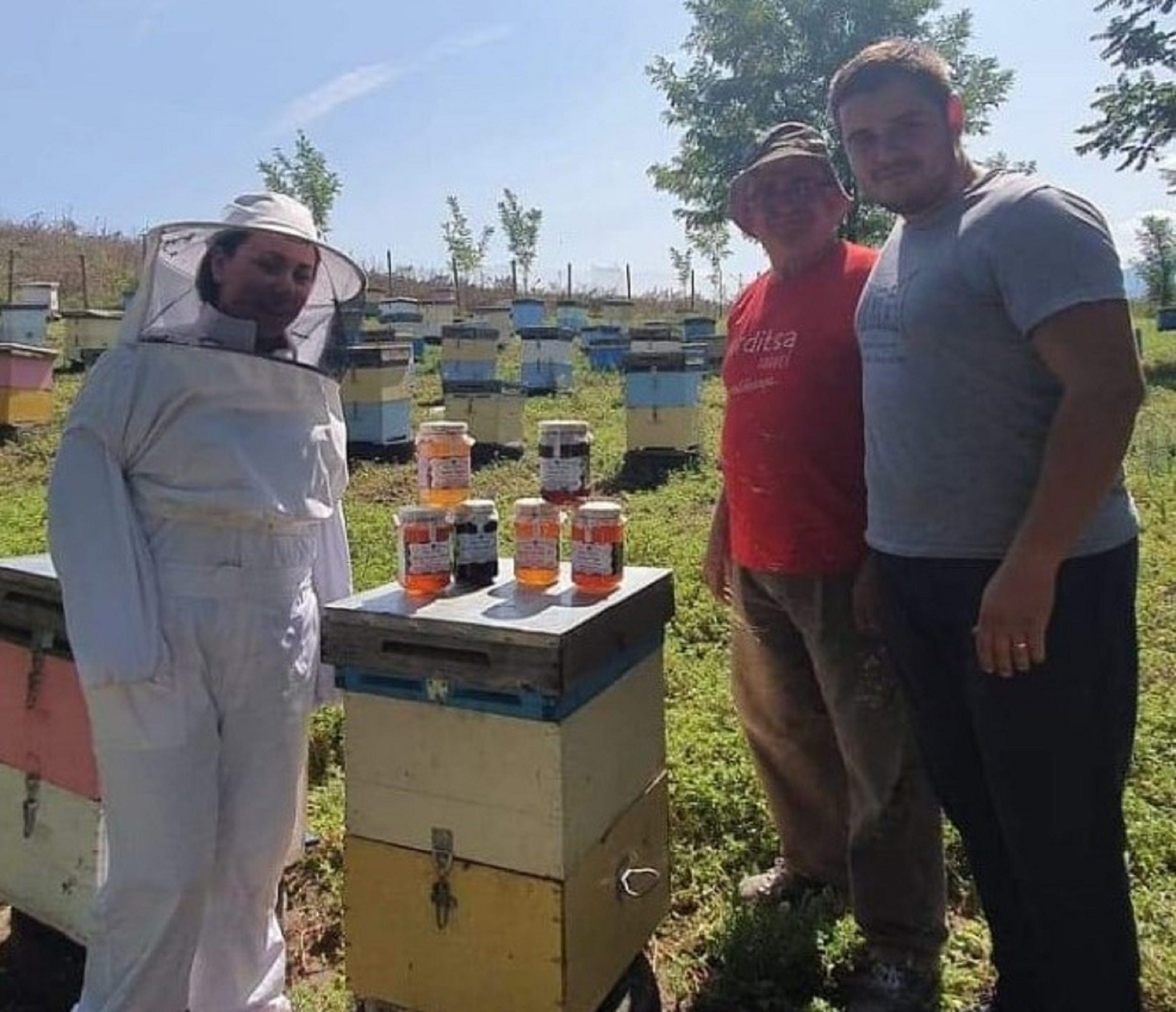 Thomas the beekeeper with colleagues amongst beehives, with honey jars sitting on central beehive.